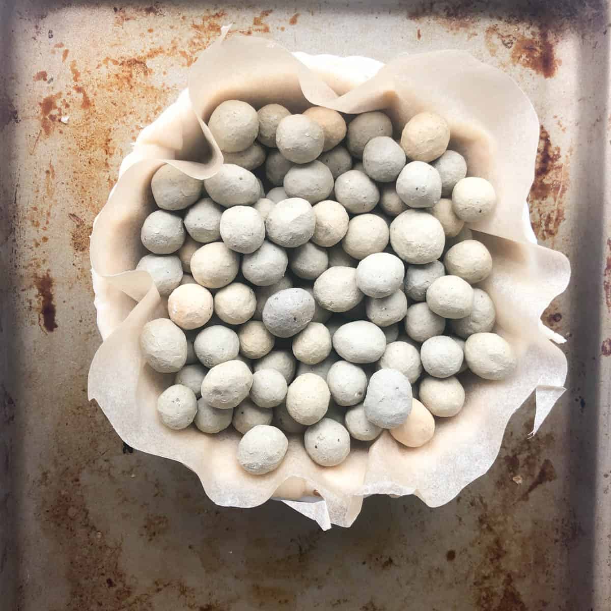 A pie crust lined with parchment paper is filled with baking beans, ready for blind baking for a Mediterranean quiche, sitting on a metal baking tray.