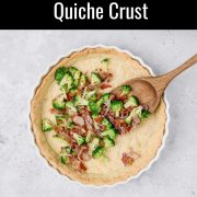 A partially filled basic quiche crust in a white dish sits on a light surface. Broccoli, red onion, and bits of meat are being spread over the crust with a wooden spoon. Text above explains how to make a flaky all-butter dough for quiche.