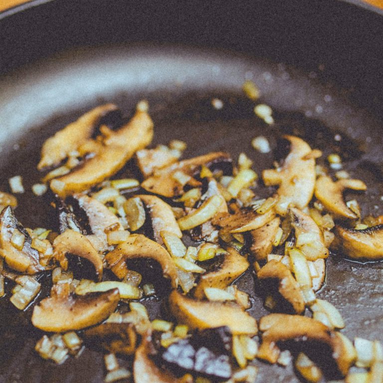 Sliced mushrooms and diced onions are being sautéed in a frying pan, with the ingredients beginning to brown and soften.