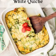 A crustless egg white spinach quiche with baked ricotta is served in a white dish using a wooden spatula. Sliced cherry tomatoes top the quiche, while plates and cutlery are arranged on a light surface nearby.